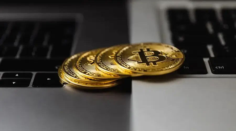 Close-up of gold Bitcoin coins placed on laptop keyboards, representing digital currency and wealth.
