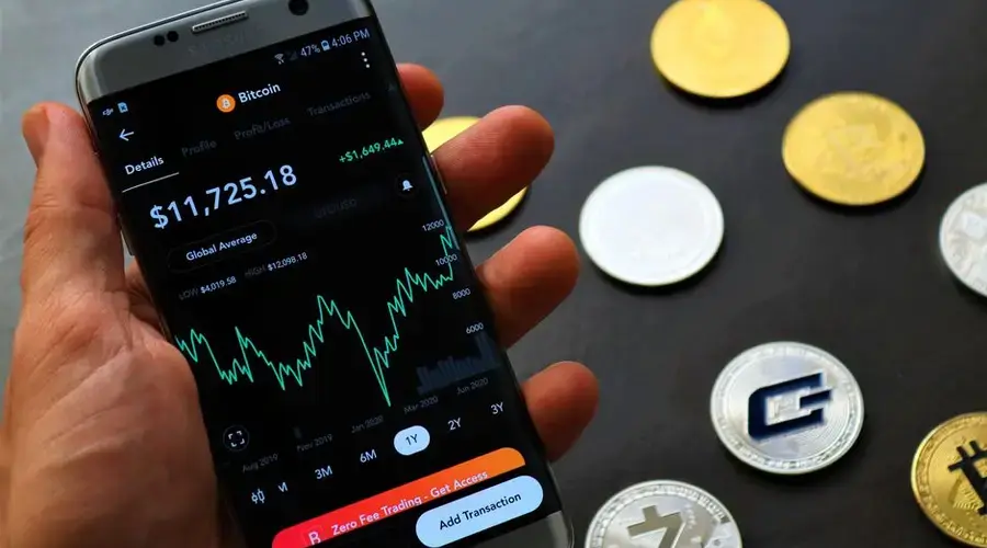 Close-up of a smartphone app showing Bitcoin trading details with crypto coins on a black surface.