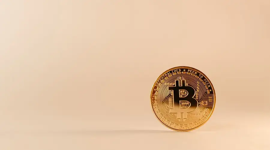 Close-up of a golden Bitcoin coin on a beige background, highlighting cryptocurrency concepts.