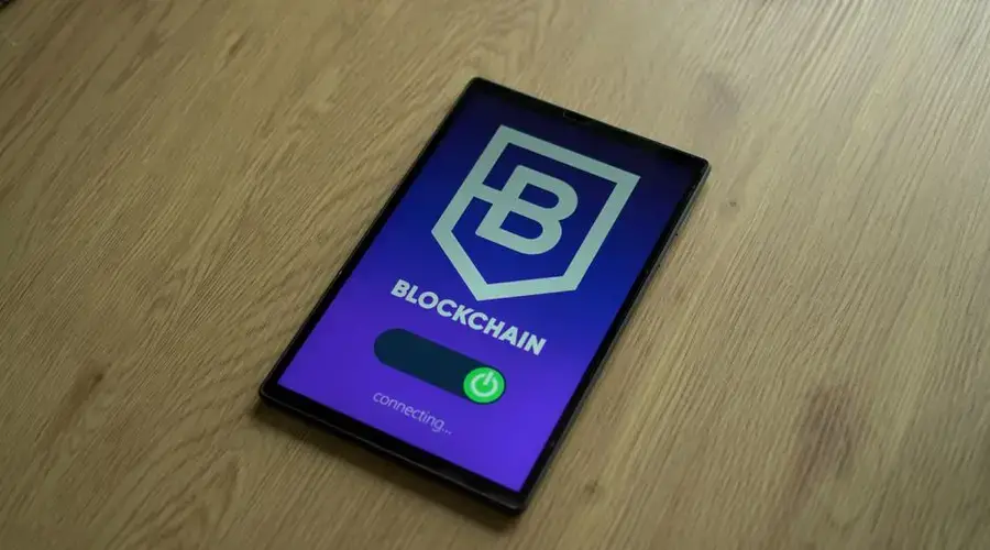 Close-up of a digital tablet showing a blockchain concept screen on a wooden surface.