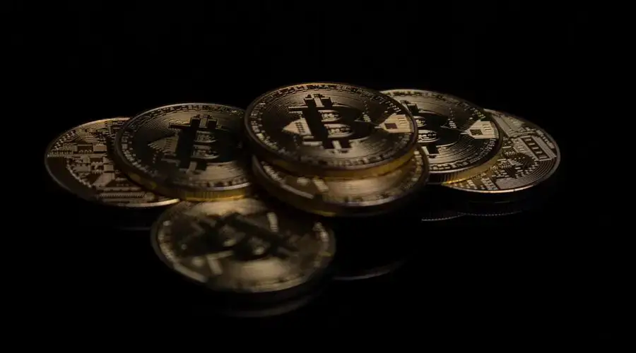 A close-up image of golden Bitcoin coins displayed on a reflective black surface.