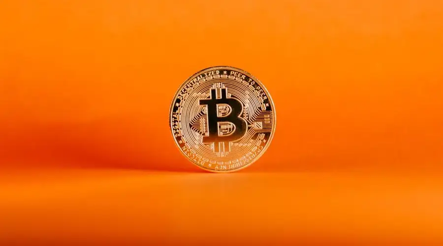 Close-up of a Bitcoin coin on an orange background, symbolizing digital cryptocurrency.
