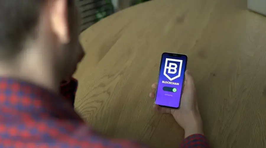 Person using a blockchain application on a smartphone indoors, showcasing technology.