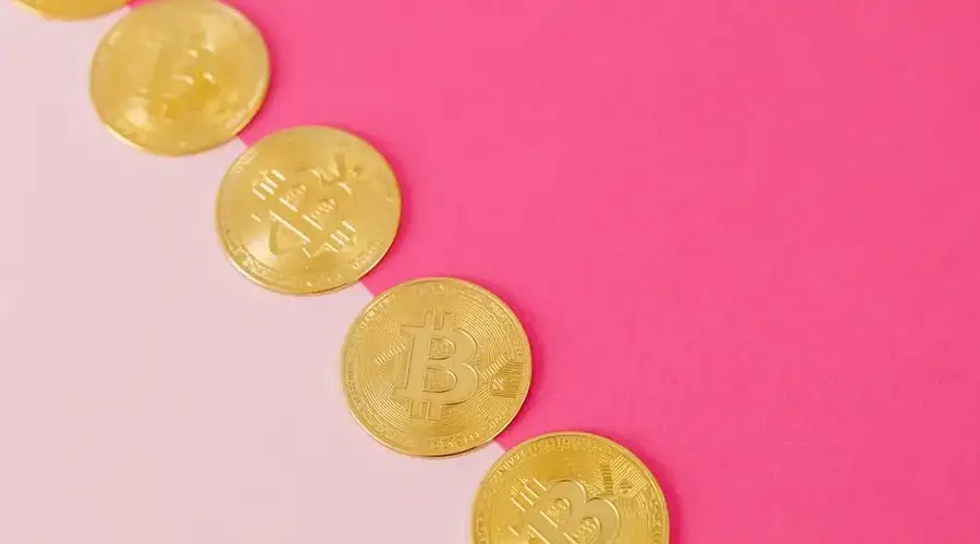 Array of gold bitcoin coins on a striking pink surface, symbolizing modern digital currency.