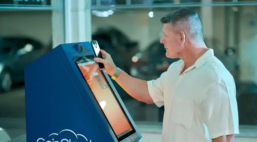 A mature man uses a CoinCloud Bitcoin ATM indoors, showcasing modern financial technology.