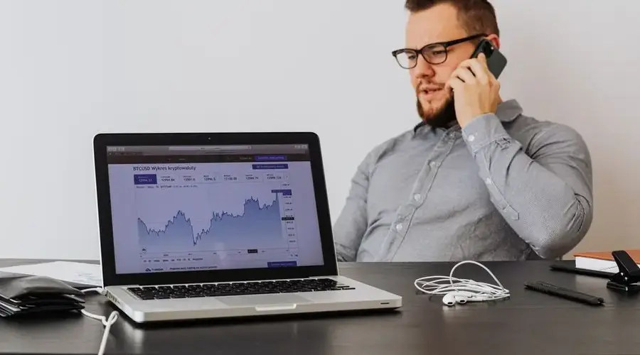 Professional in office analyzing cryptocurrency trends on laptop while on phone call.