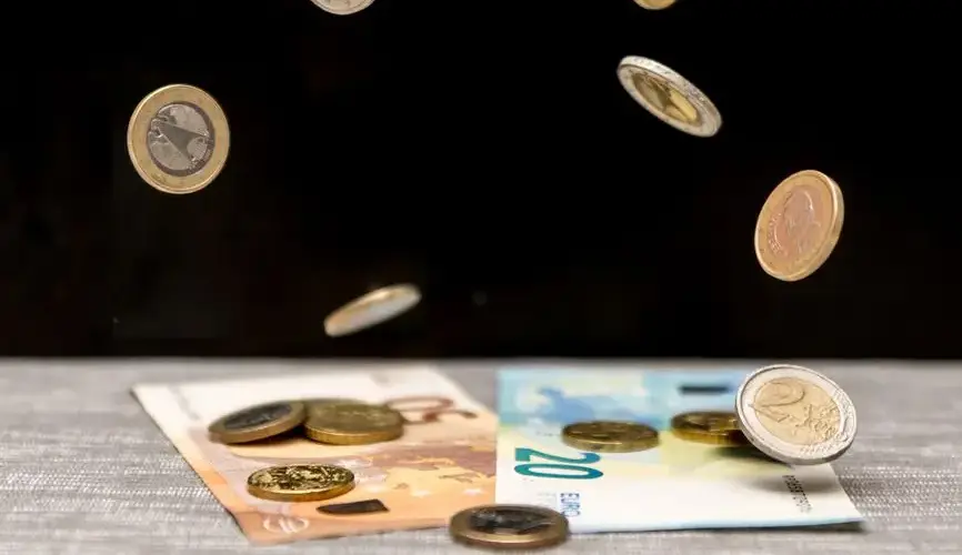Dynamic image of euro coins and banknotes cascading onto a table against a black background.