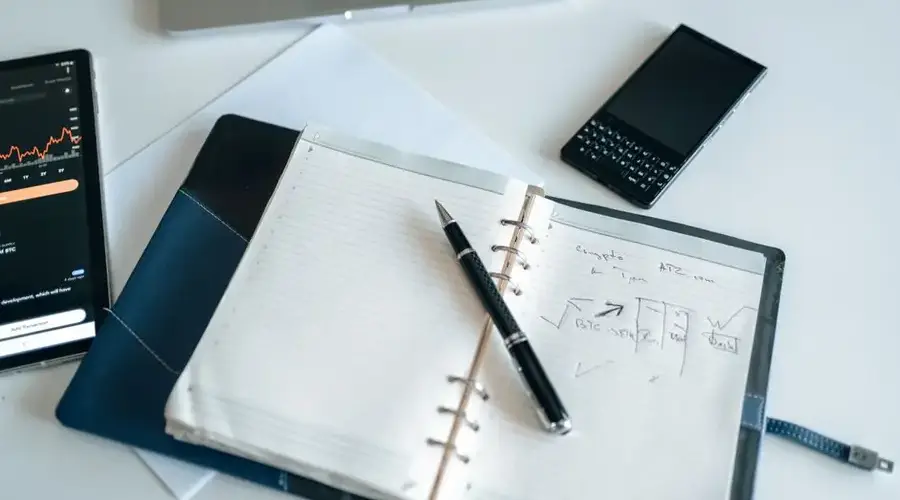 Flat lay of a workspace with a notebook, pen, and electronic devices, ideal for productivity.