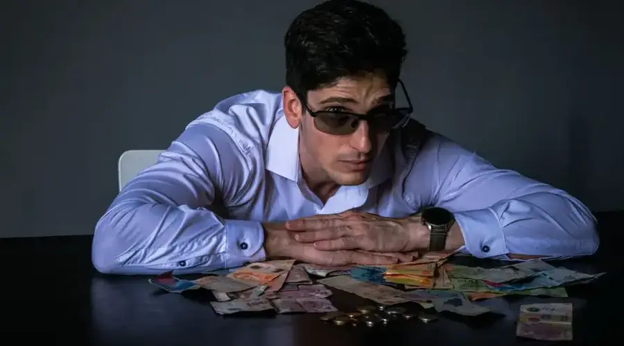 Portrait of a man in sunglasses leaning over a table covered with various currencies.