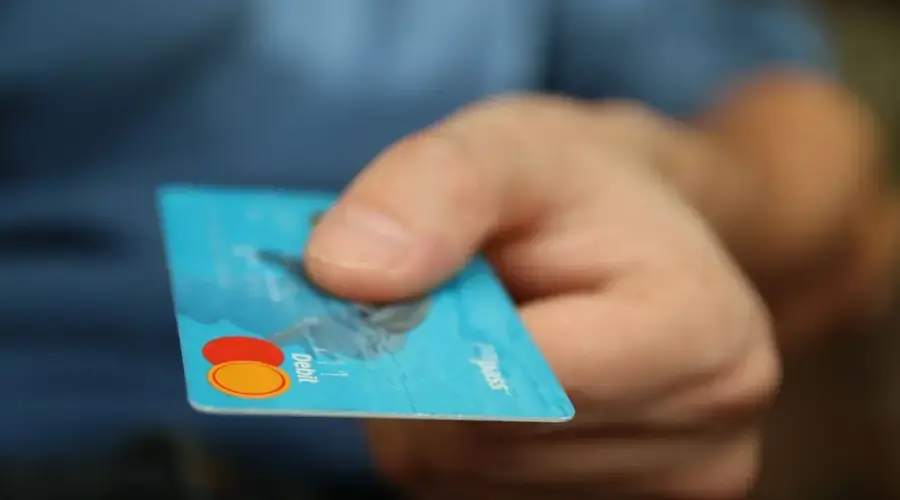 A close-up shot of a hand offering a blue debit card for payment.