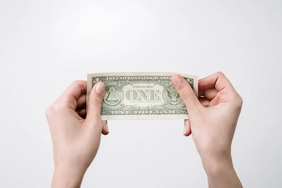 A close-up image of hands holding a one dollar bill, symbolizing finance and economy.