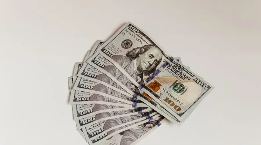 Crisp US hundred dollar bills fanned out on a clean white surface, representing wealth and finance.