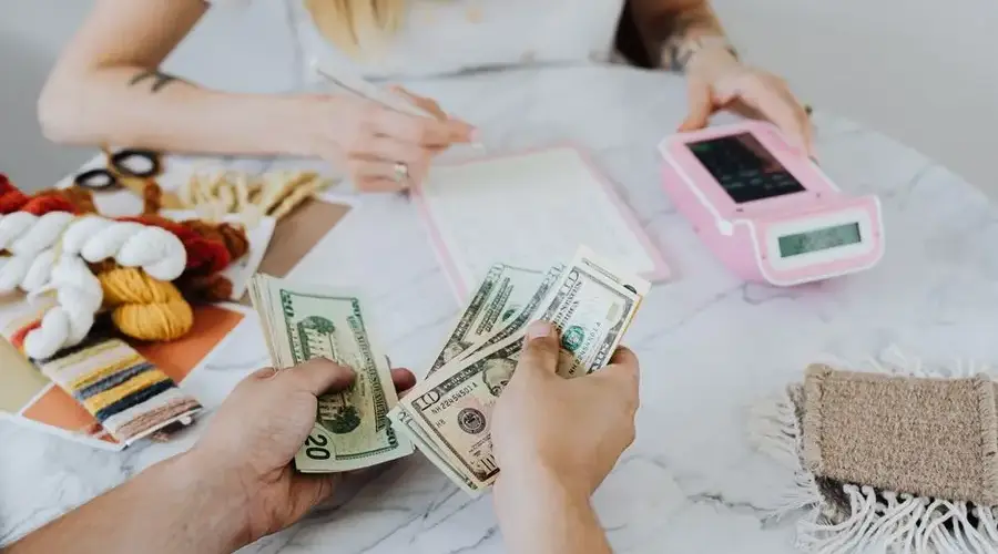 Two people handling cash and budgeting with a calculator and notebook at a table.