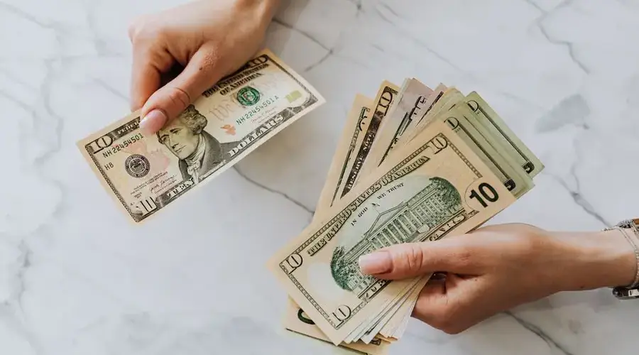 Close-up of hands counting US dollar bills on a marble background, highlighting financial theme.