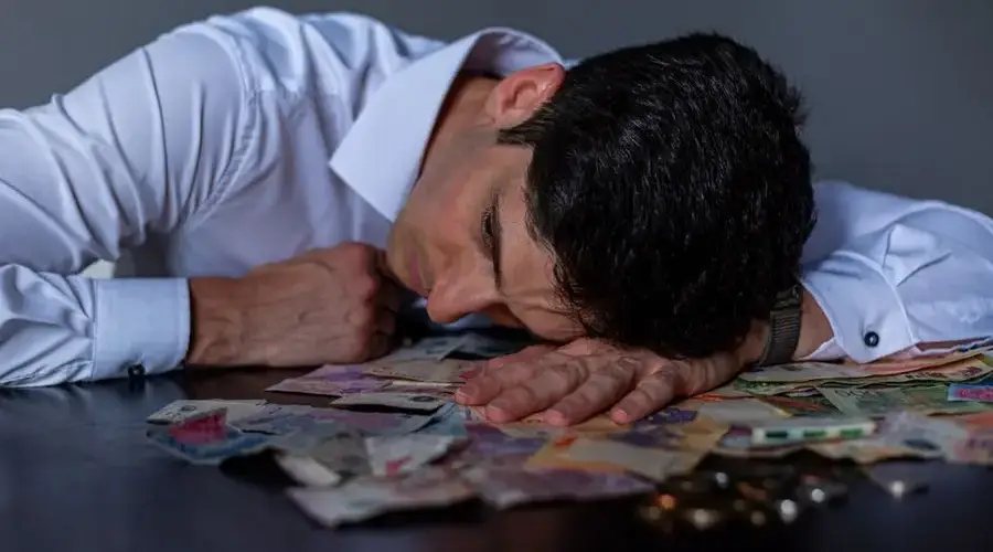 Man in stress resting on table covered with Argentine pesos symbolizing financial hardship.