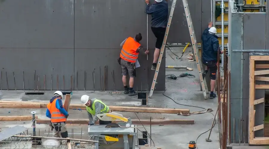 Construction workers building a concrete structure, wearing safety gear on an active site.