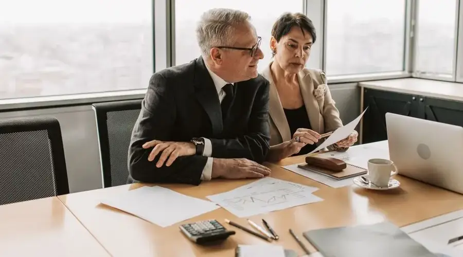 Two business professionals analyzing financial papers in a modern office setting.