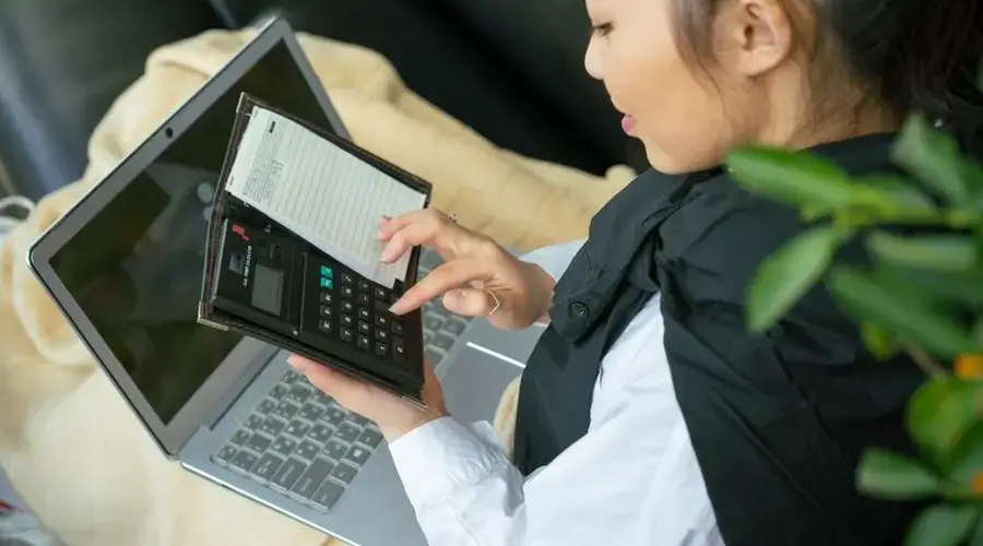 Focused young woman calculating finances on laptop indoors.