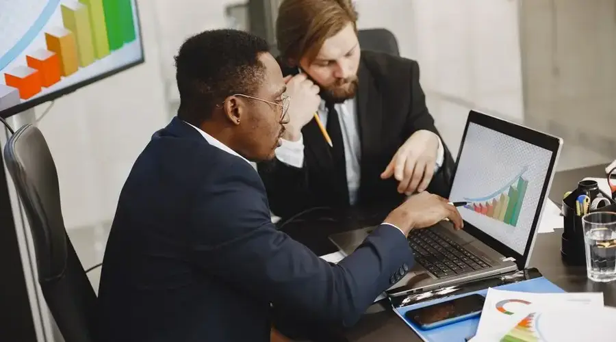 Two business professionals working on growth charts using laptop in an office setting.