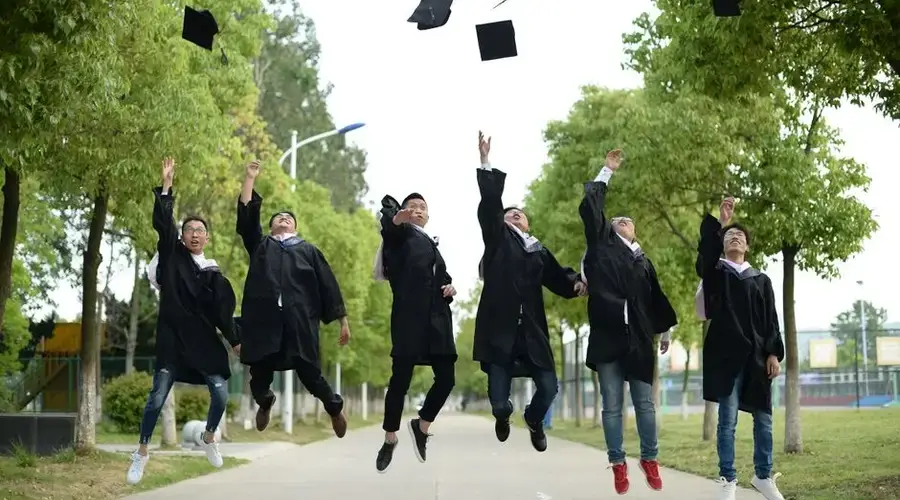 A joyful group of graduates throwing caps in the air during a graduation ceremony in a park setting.