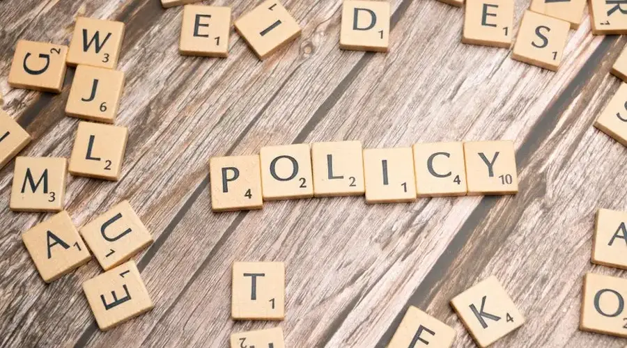 Scrabble letter tiles on a wooden background forming the word "Policy".