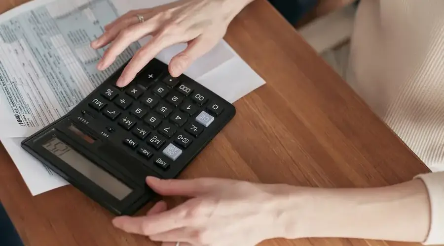 Close-up of a woman using a calculator and reviewing bills at home.
