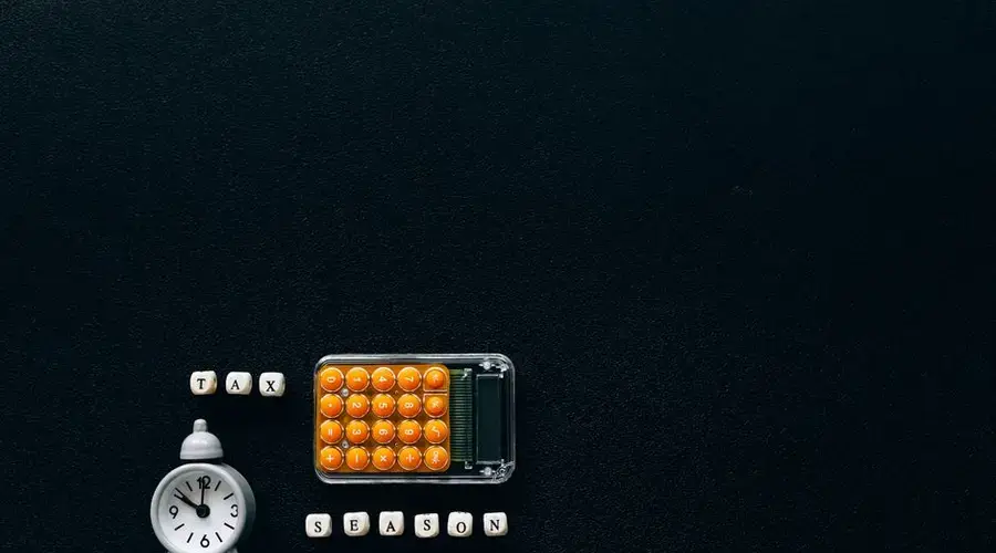 Flat lay of a tax season theme with a clock and calculator on a dark background.