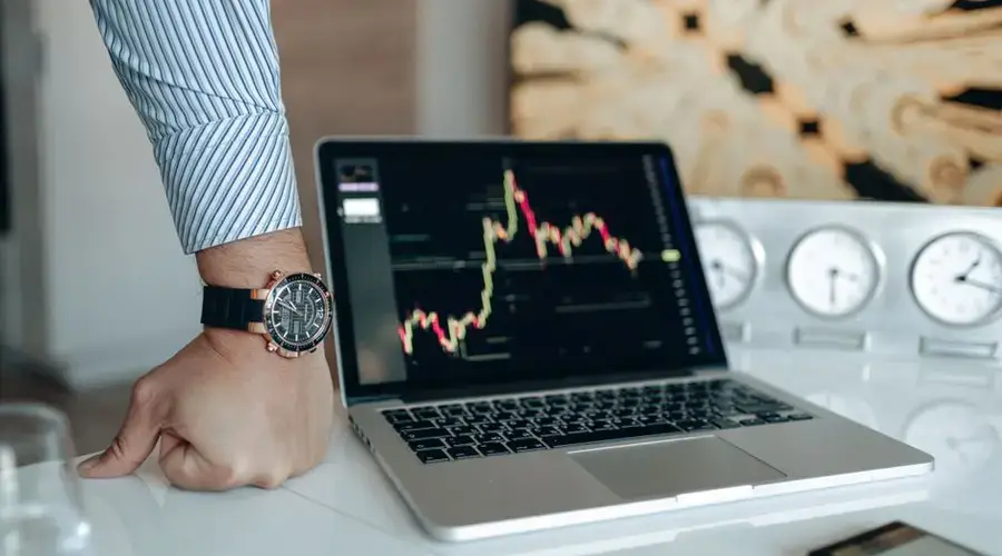 A sophisticated workspace featuring a laptop with a stock chart and a watch on a man's wrist.