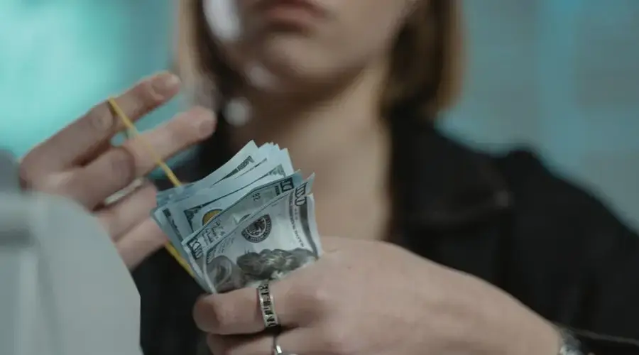 Close-up of a person counting US dollar bills indoors, focusing on finance and money handling.