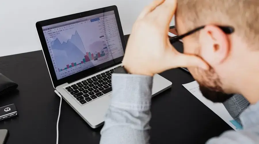 Over the shoulder view of a man analyzing financial data on a laptop screen.