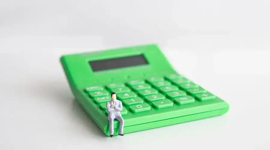 Conceptual image of a miniature businessman sitting on a green calculator, symbolizing finance and calculation.