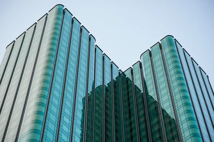 Vertical view of a modern skyscraper featuring glass facade and reflection under clear sky.