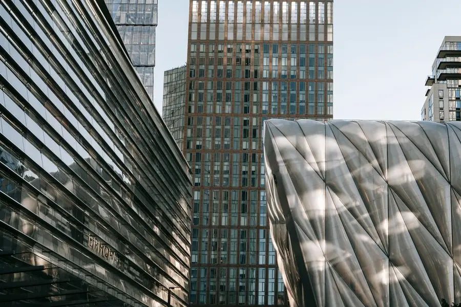 Contemporary geometric buildings with glass wall and unusual design located on street in downtown against skyscraper in modern district in city