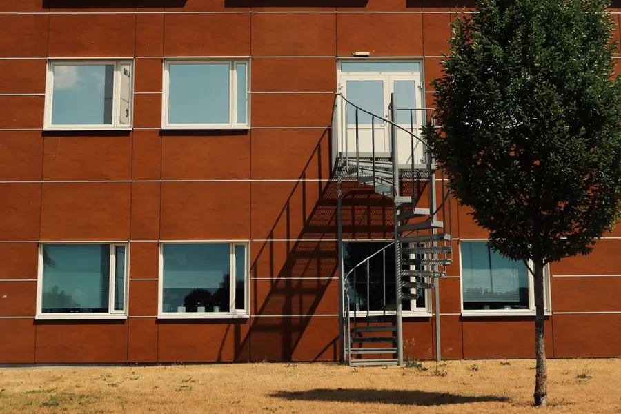 Modern apartment facade in Jönköping, Sweden, featuring a brown facade with spiral staircase and tree.