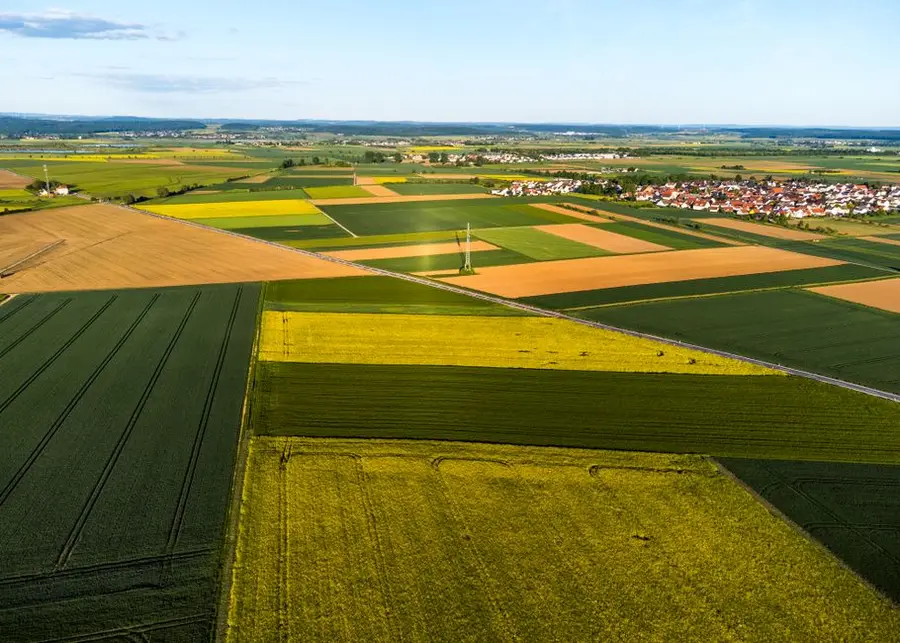 Aerial image showcasing vibrant patchwork farmland with a village in the distance, under a clear blue sky.