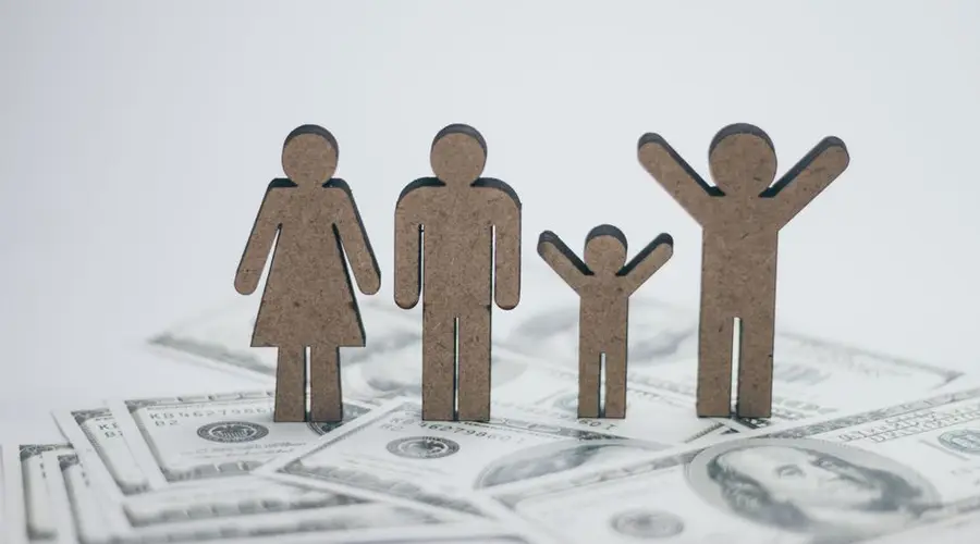 Wooden family figurines on dollar bills symbolizing financial stability.