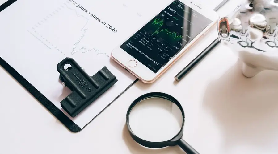 Flat lay of financial tools including a smartphone with stock data, magnifying glass, and chart.