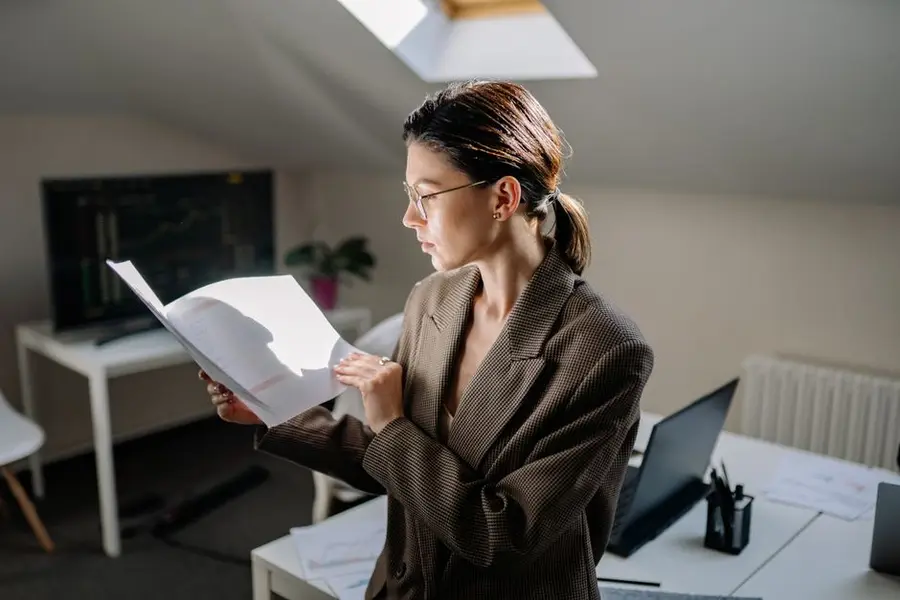 Professional woman in glasses reviewing financial documents at her office desk.