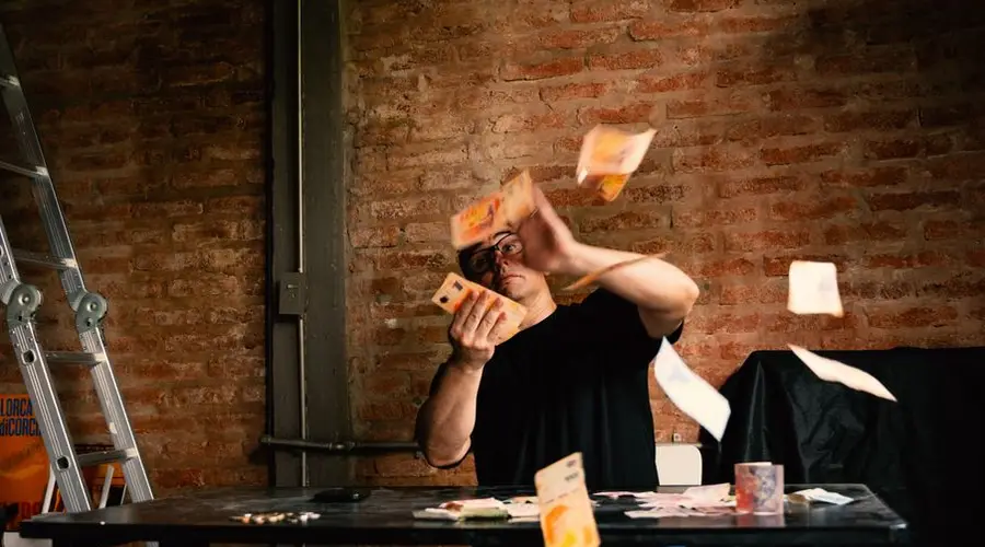 Man sitting at a table with Argentine pesos flying around in industrial interior.