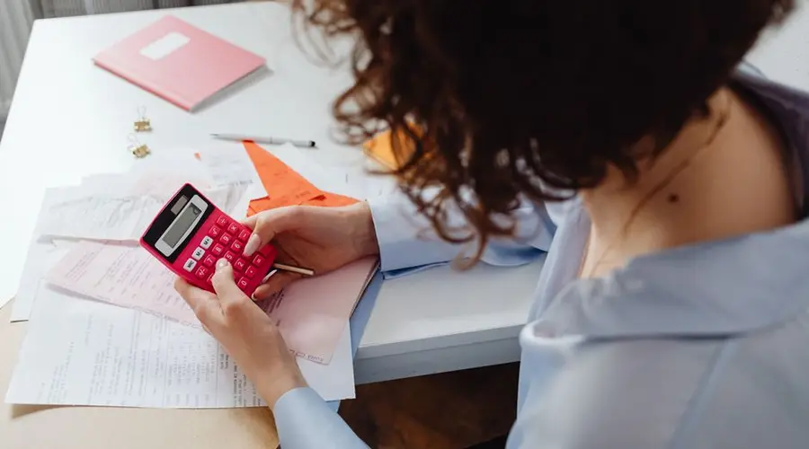 Woman calculating expenses with documents and calculator at work desk.