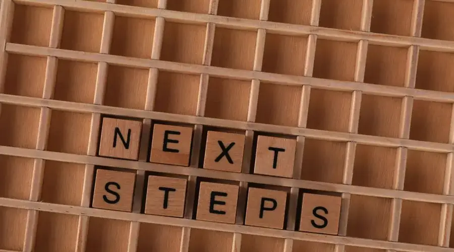Flat lay of wooden letter blocks spelling 'Next Steps', inspiring progress and motivation.