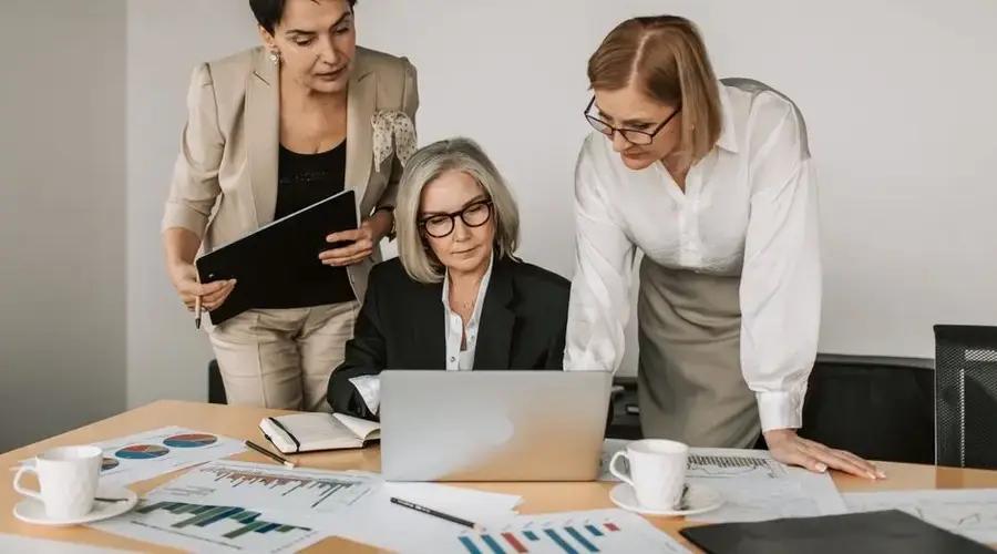 Three women in a business meeting, discussing strategy with charts and laptop.
