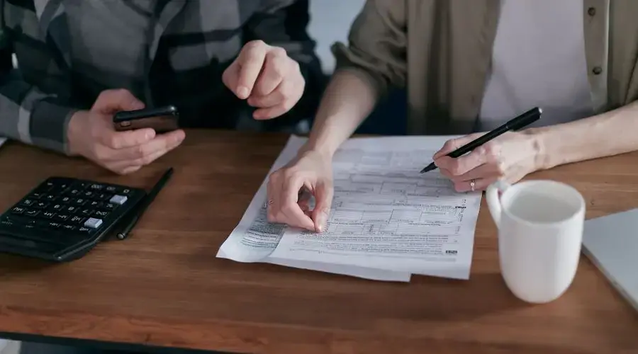 Couple managing finances at home with a calculator, smartphone, and documents.
