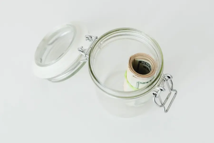 Close-up shot of rolled US dollar bills inside a glass jar on a white surface.