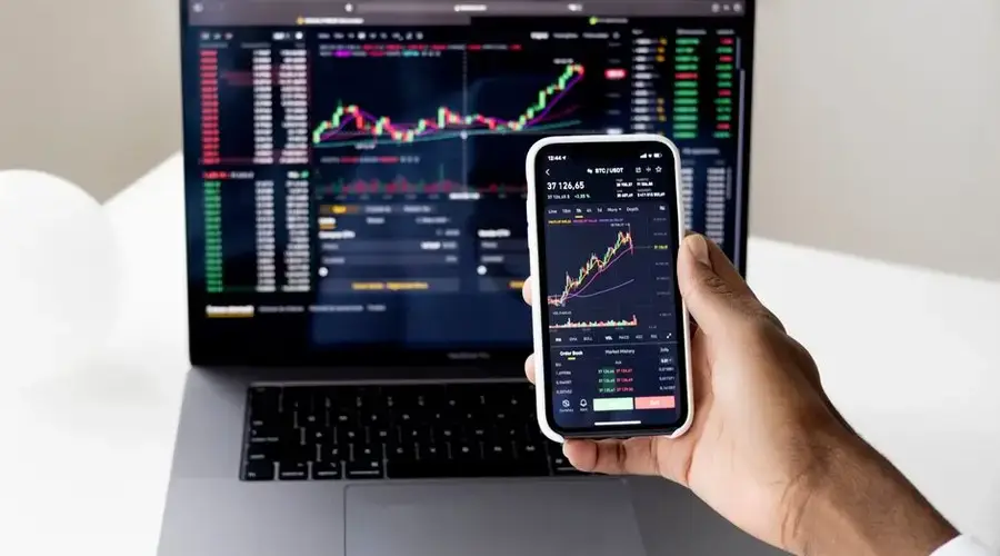 Person checking stock market graphs on laptop and smartphone, focusing on financial data.