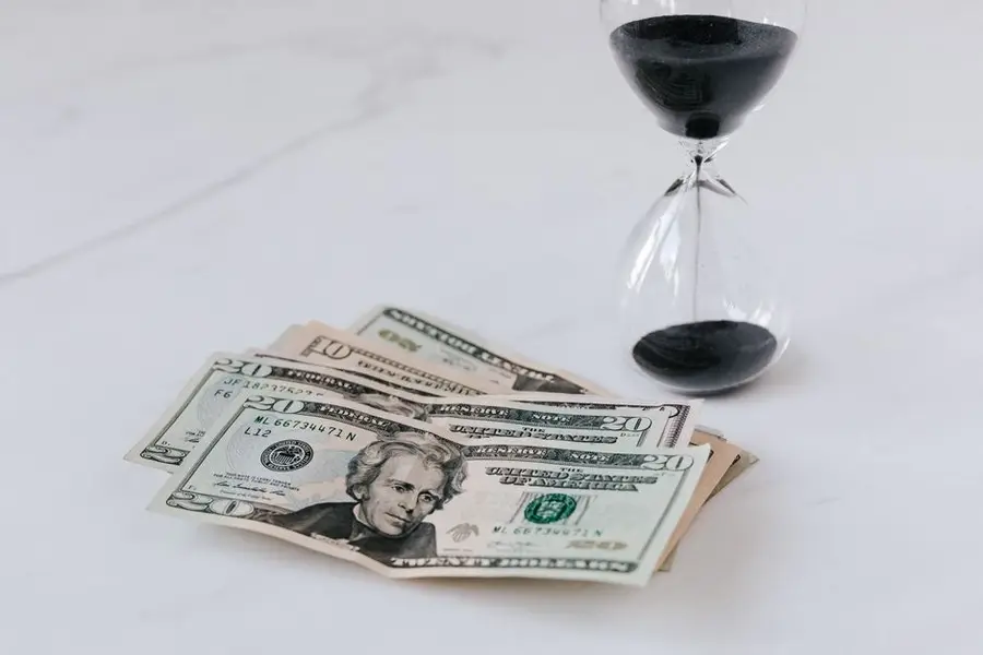 From above of transparent glass with black sand on white table and pile of paper money with image of president