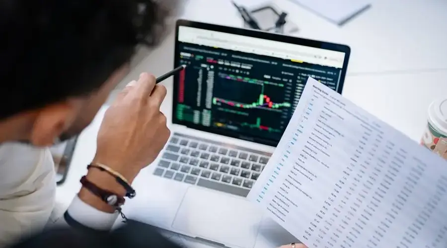 A professional analyzing stock market data on a laptop screen with financial documents.