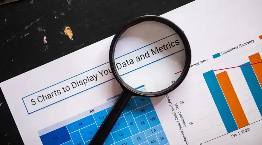 Close-up of a magnifying glass over financial data charts and metrics on printed paper.