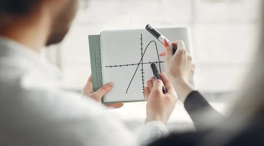 Two professionals discussing a parabola graph on a notebook, promoting teamwork and collaboration.