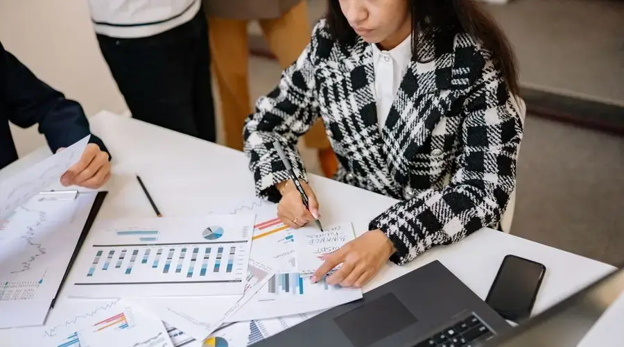 Businesswoman reviewing graphs and charts with colleagues, analyzing financial data in a modern office setting.